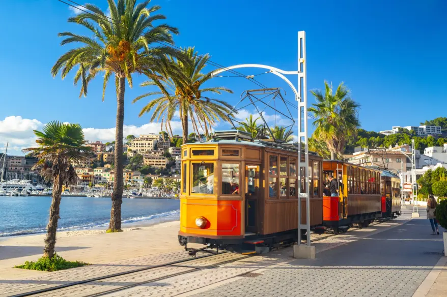 Historische Holzstraßenbahn in Orange und Braun auf der von Palmen gesäumten Uferpromenade von Port de Sóller
