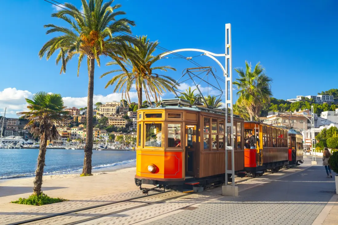 Historische Holzstraßenbahn in Orange und Braun auf der von Palmen gesäumten Uferpromenade von Port de Sóller