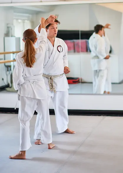 Karate-Training im Dojo: Trainer korrigiert die Deckung einer Schülerin, beide im weißen Gi