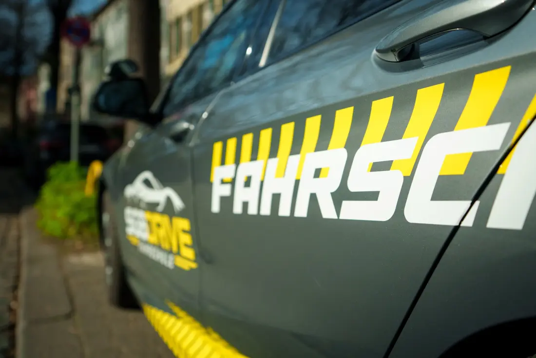 Anthrazitfarbener Fahrschulwagen von SG8 Drive in Seitenansicht, mit Logo und gelb-weißer Beschriftung „Fahrschule“ auf der Tür